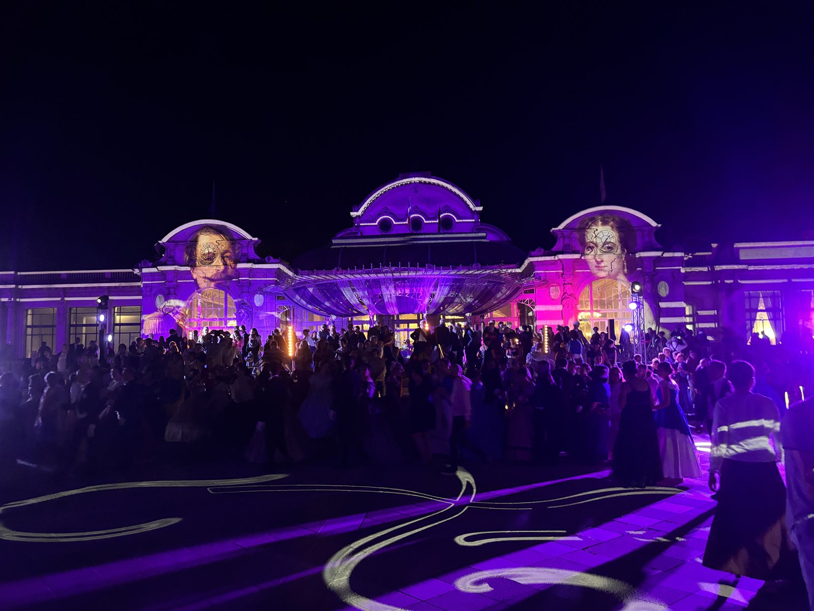 Danseurs en costumes devant le Palais des Congrès de Vichy illuminé de projections violettes lors de la soirée Eugénie × Bridgerton
