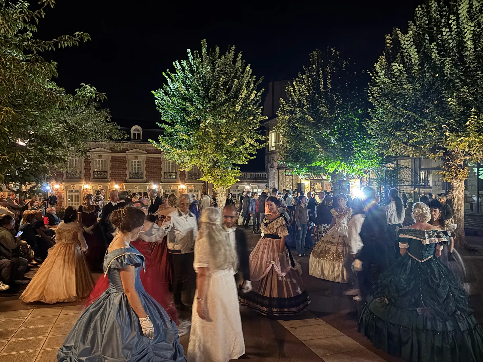 Danseurs en robes de bal et habits dans la cour du Musée de la Dentelle de Chantilly, éclairée à la nuit tombée