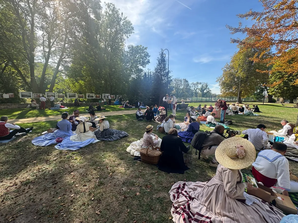 Adhérents en costumes historiques installés en petits groupes sur des nappes dans le parc de Chantilly