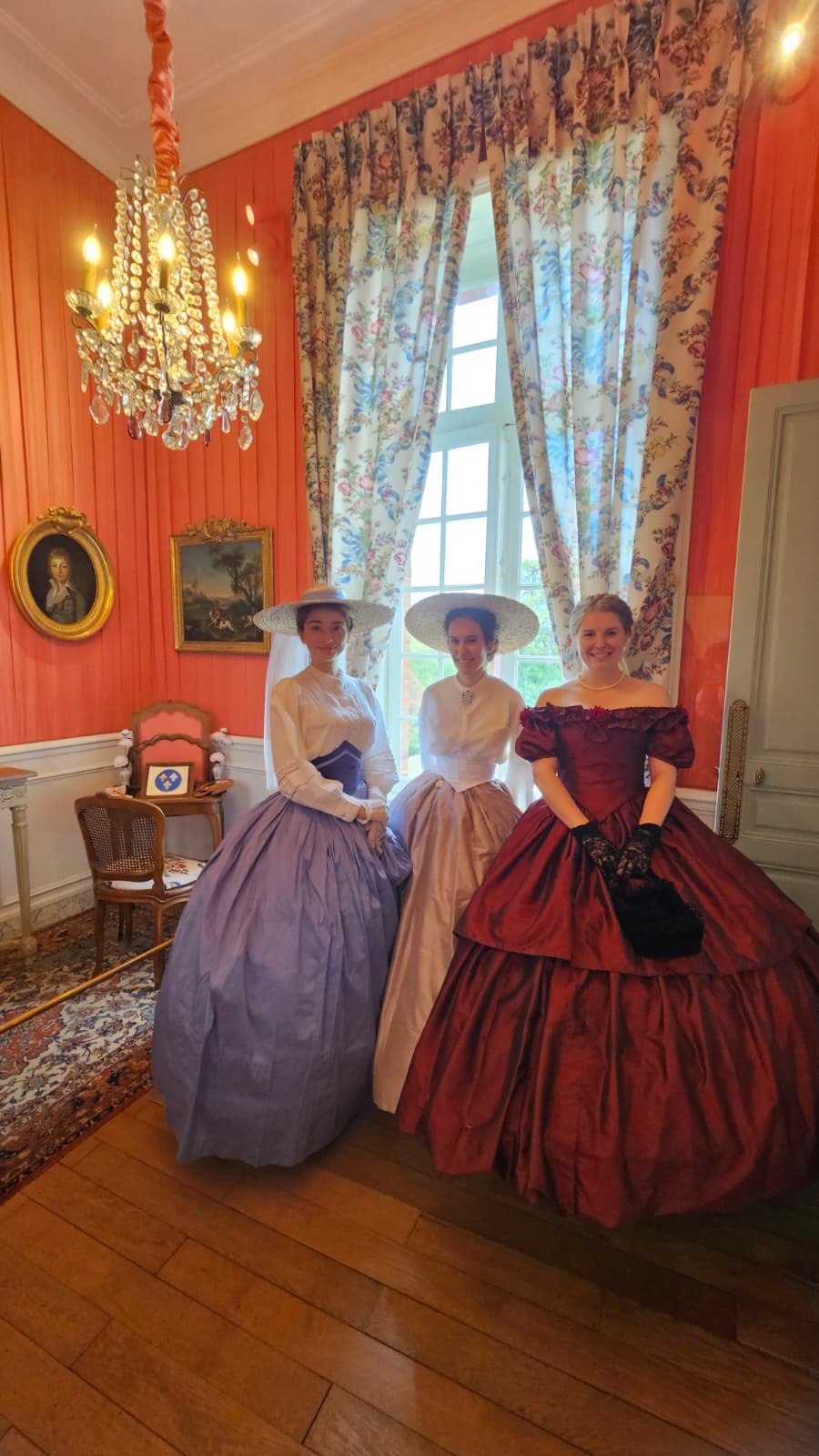 Trois participantes en robes à crinoline posant dans un salon du Château de Breteuil